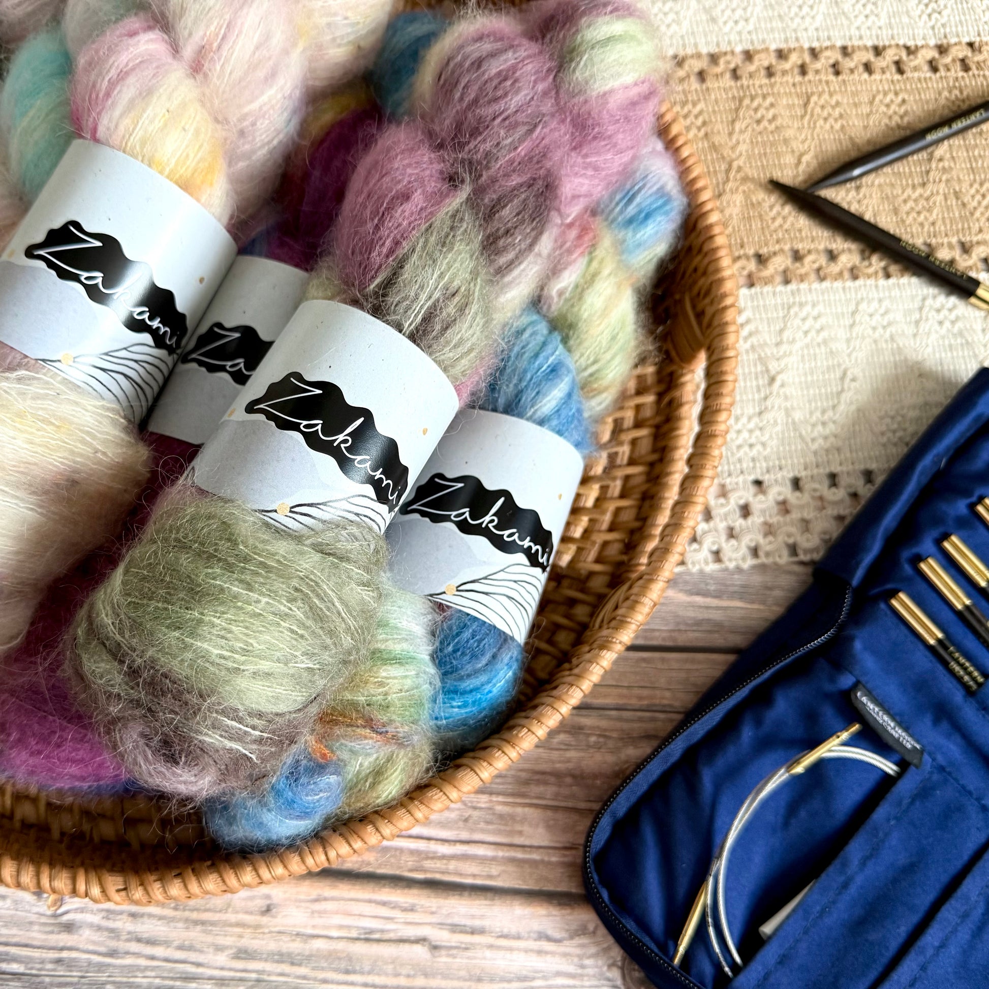 Yarn skeins in a basket with a navy blue knitting set on a wooden surface